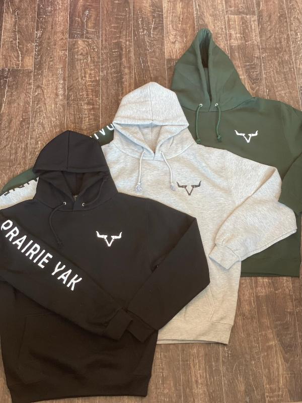 Branded black, gray, and green hoodies laid on a wooden floor.