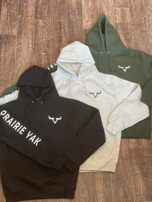 Branded black, gray, and green hoodies laid on a wooden floor.